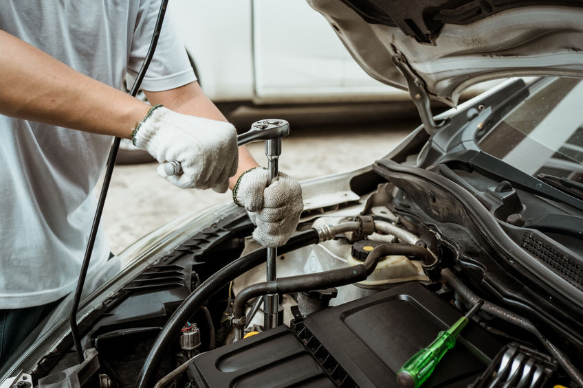 Person using a ratchet wrench to repair a car engine, wearing white gloves. A screwdriver is placed nearby.