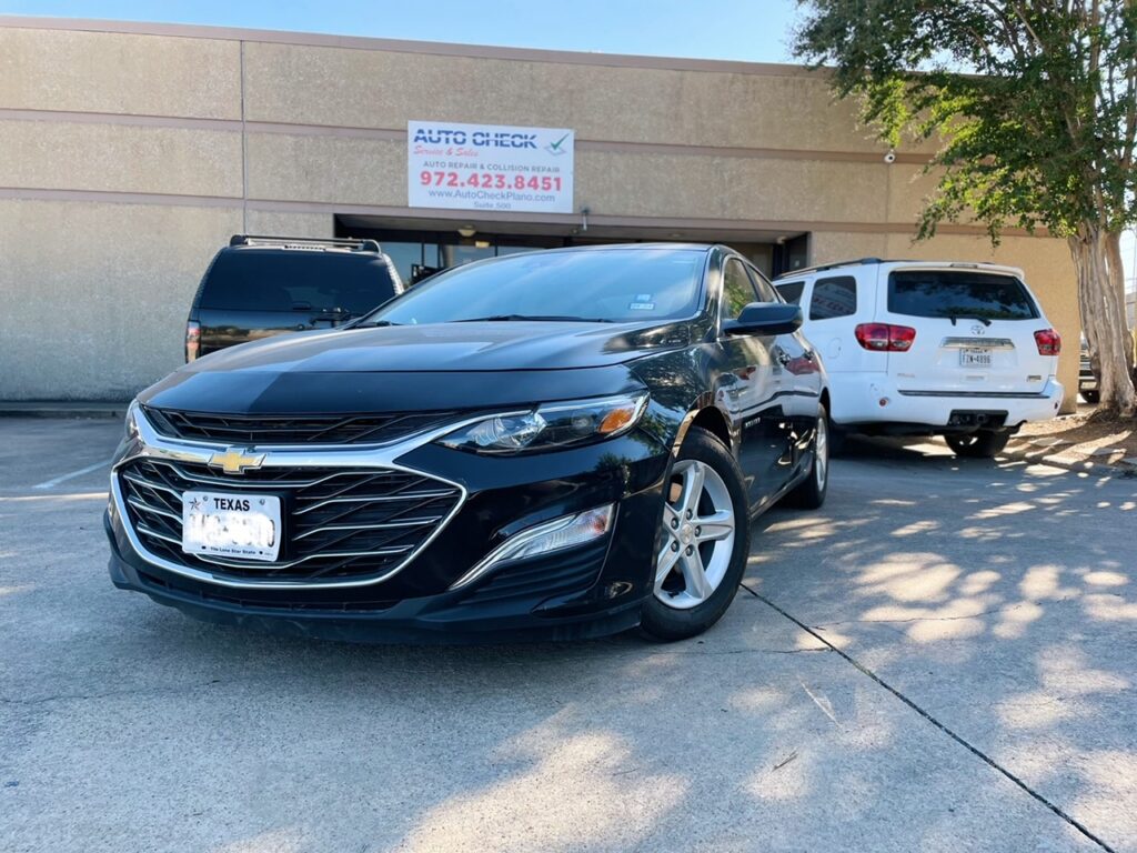 Black Chevrolet sedan parked in front of an auto service center with a white SUV nearby; building features are visible.